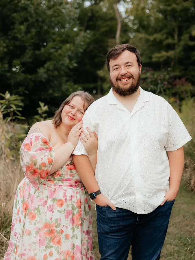 Me with my wife Roxanne posing for one of our engagement photos in front of a garden and forest.